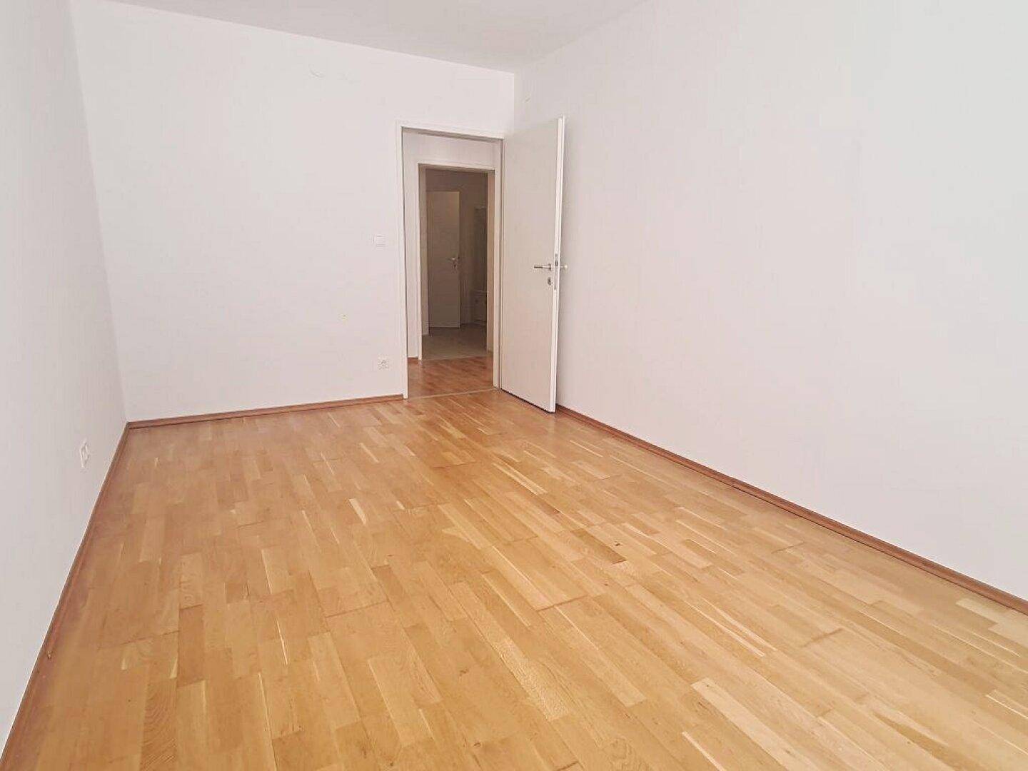Geräumiges Zimmer mit Parkettboden und offenem Durchgang zu einem angrenzenden Raum.