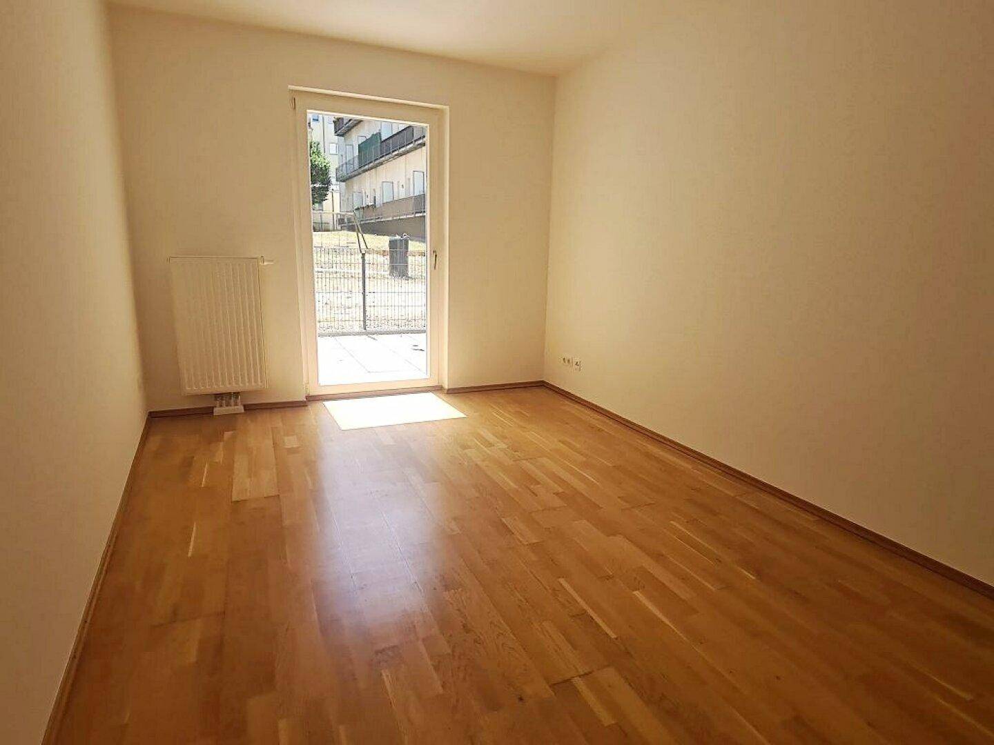 Helles Zimmer mit Parkett und Zugang zum Außenbereich, bietet eine angenehme Wohnatmosphäre.