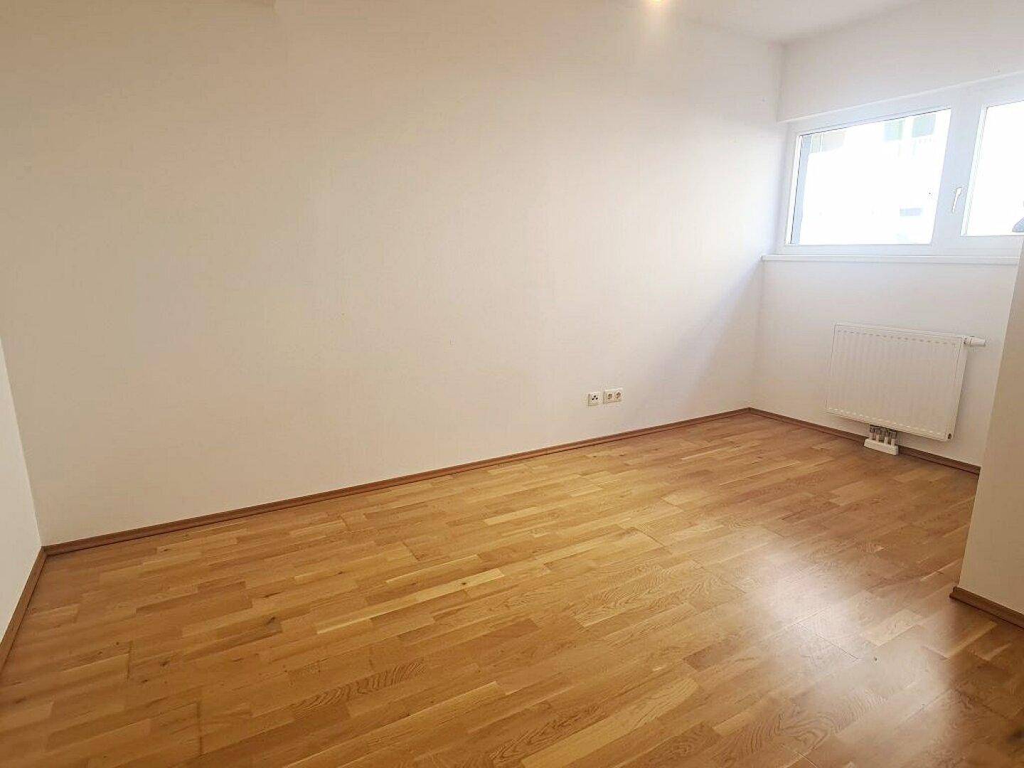 Helles Zimmer mit Parkettboden und Fenster, das für ausreichend Tageslicht sorgt.