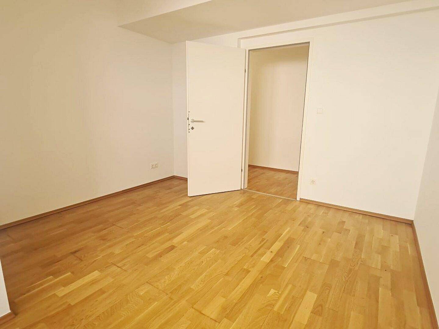 Leeres Zimmer mit Parkettboden und offenem Zugang zu einem weiteren Raum, ideal für individuelle Gestaltung.
