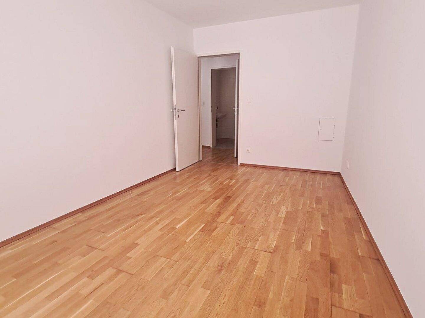Schlichtes Zimmer mit Parkettboden und weiß gestrichenen Wänden, bietet vielseitige Nutzungsmöglichkeiten.