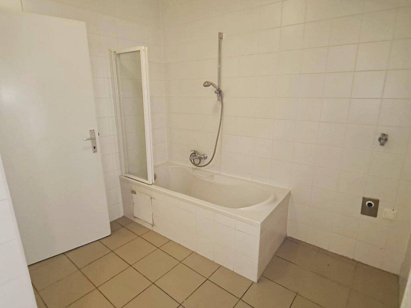 Badezimmer mit Badewanne, Duschvorrichtung und weiß gefliesten Wänden und Boden.