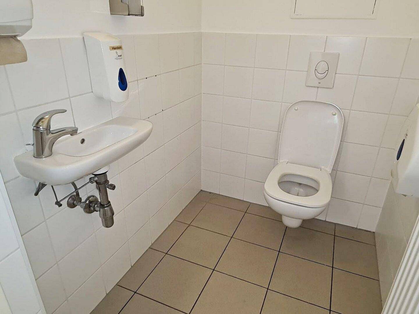Separate Toilette mit Wand-WC und kleinem Handwaschbecken, komplett gefliest.