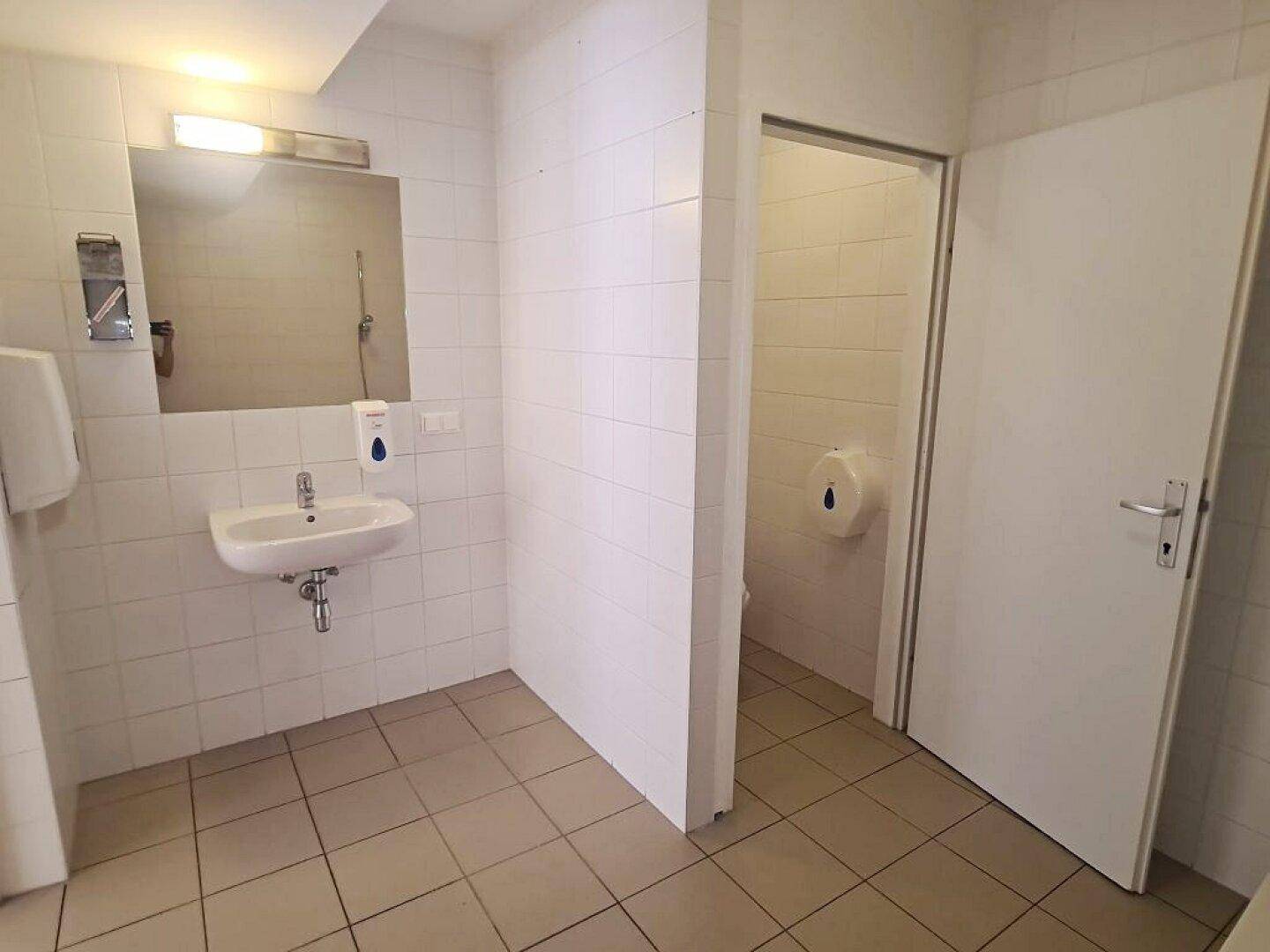 Gefliestes Badezimmer mit Waschbecken, Spiegel und Zugang zu einer separaten Toilette.