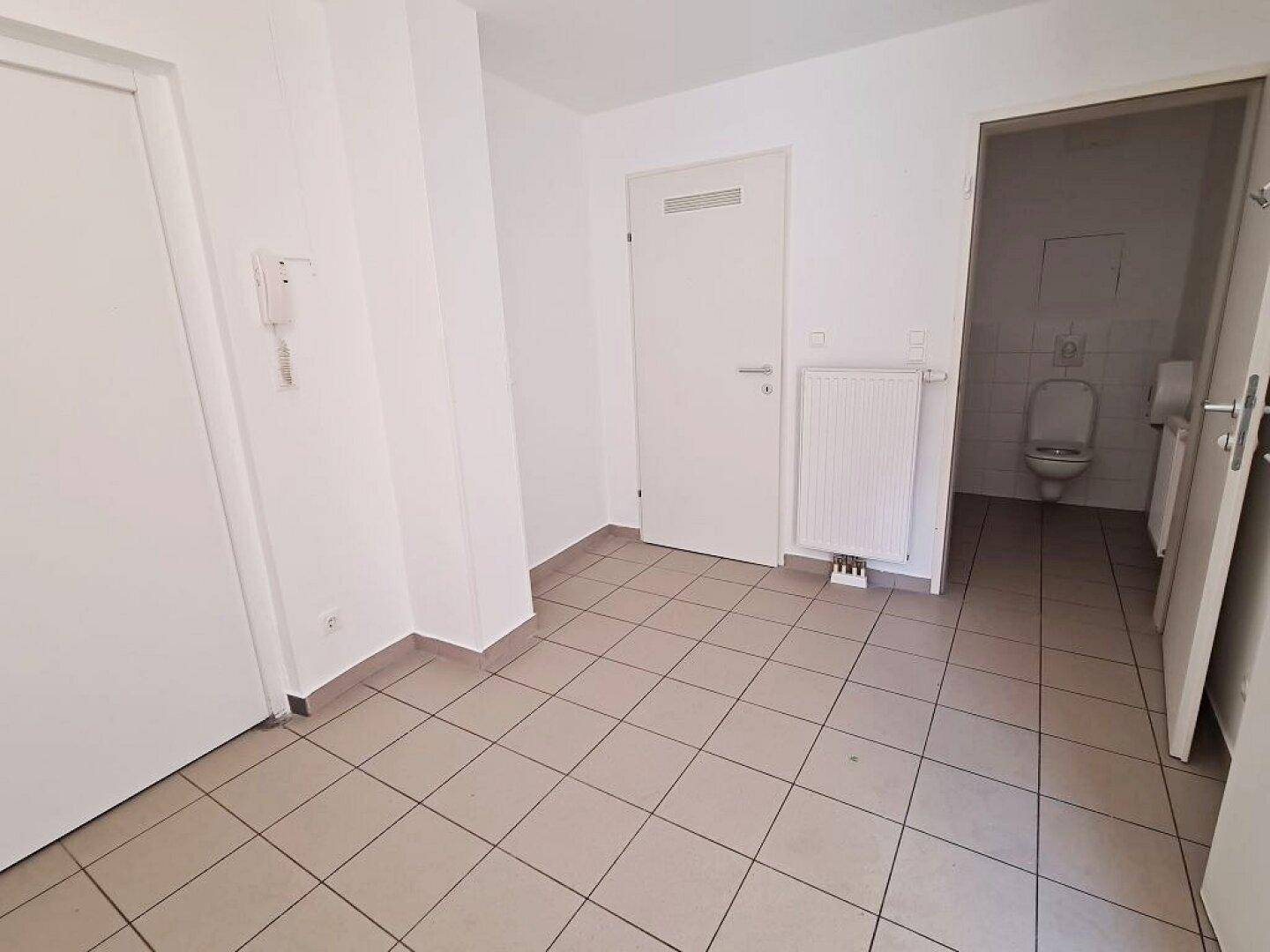Eingangsbereich mit Fliesenboden, Gegensprechanlage und Zugang zu verschiedenen Räumen, inklusive WC.