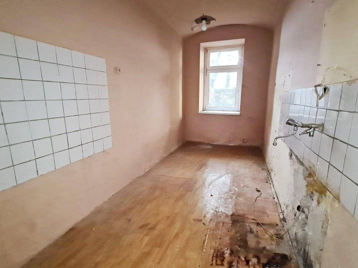 Leere Küche in renovierungsbedürftigem Zustand mit Fliesen und Holzboden, bereit zur Sanierung.