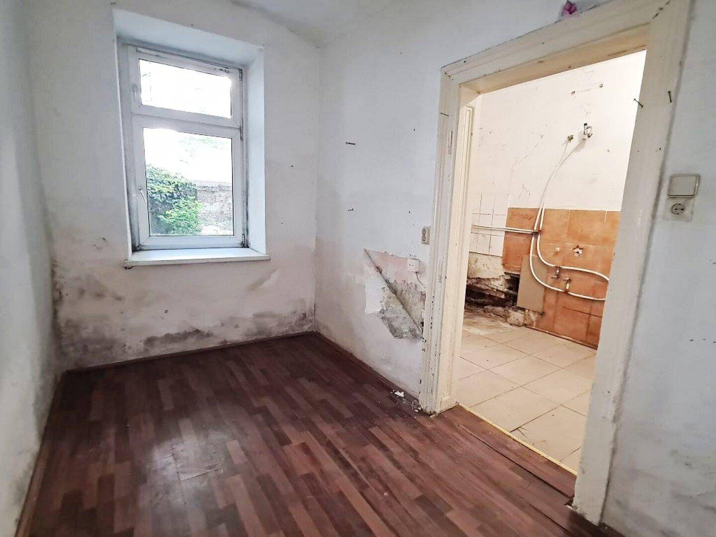 Kleines Zimmer mit Holzboden und Fenster, das eine umfassende Renovierung erfordert.