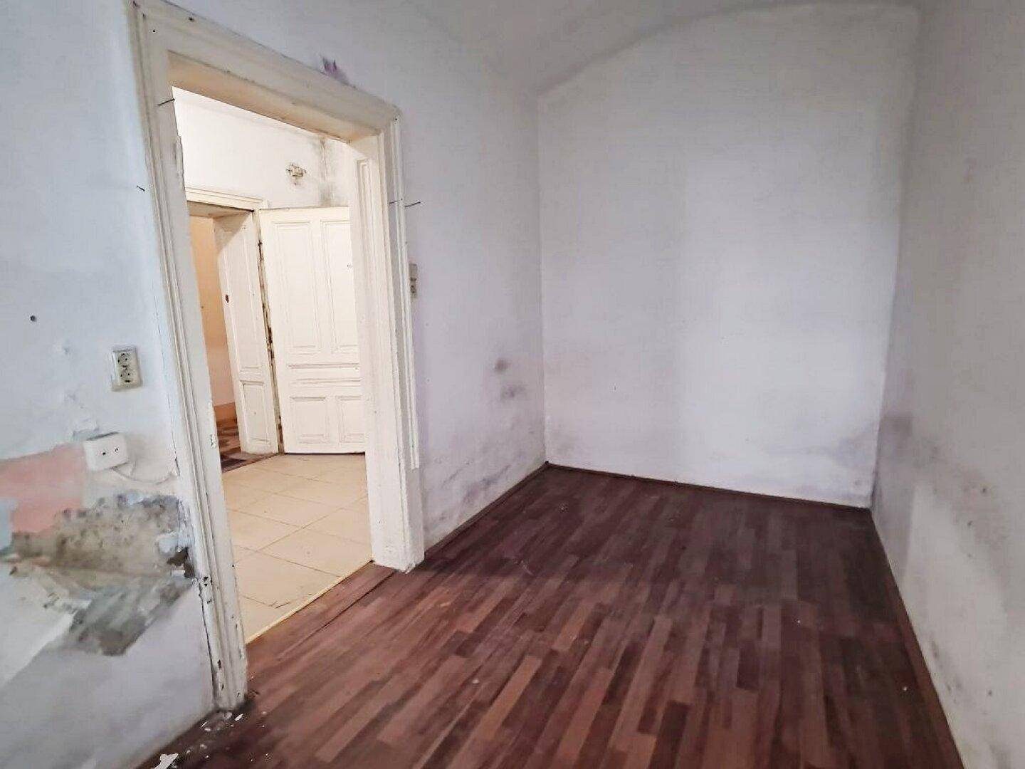 Leeres Zimmer mit Holzboden und Türrahmen, bereit für eine vollständige Sanierung.