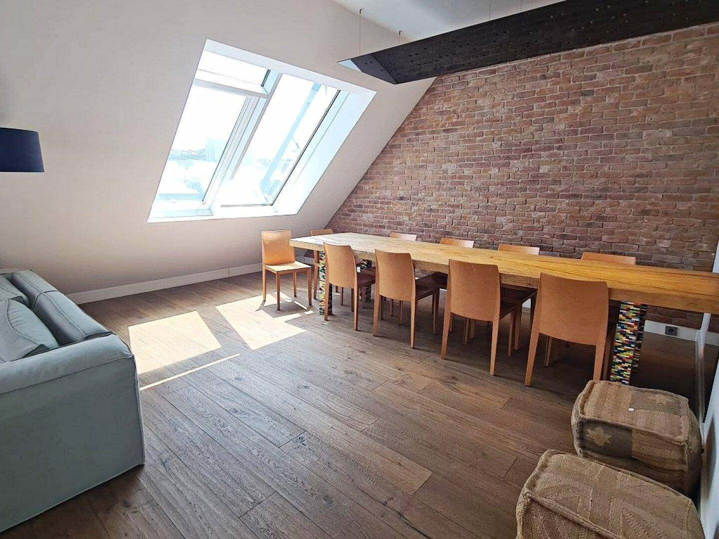 Heller Essbereich mit Holztisch, Stühlen und großen Dachfenstern, die viel Licht hereinlassen.