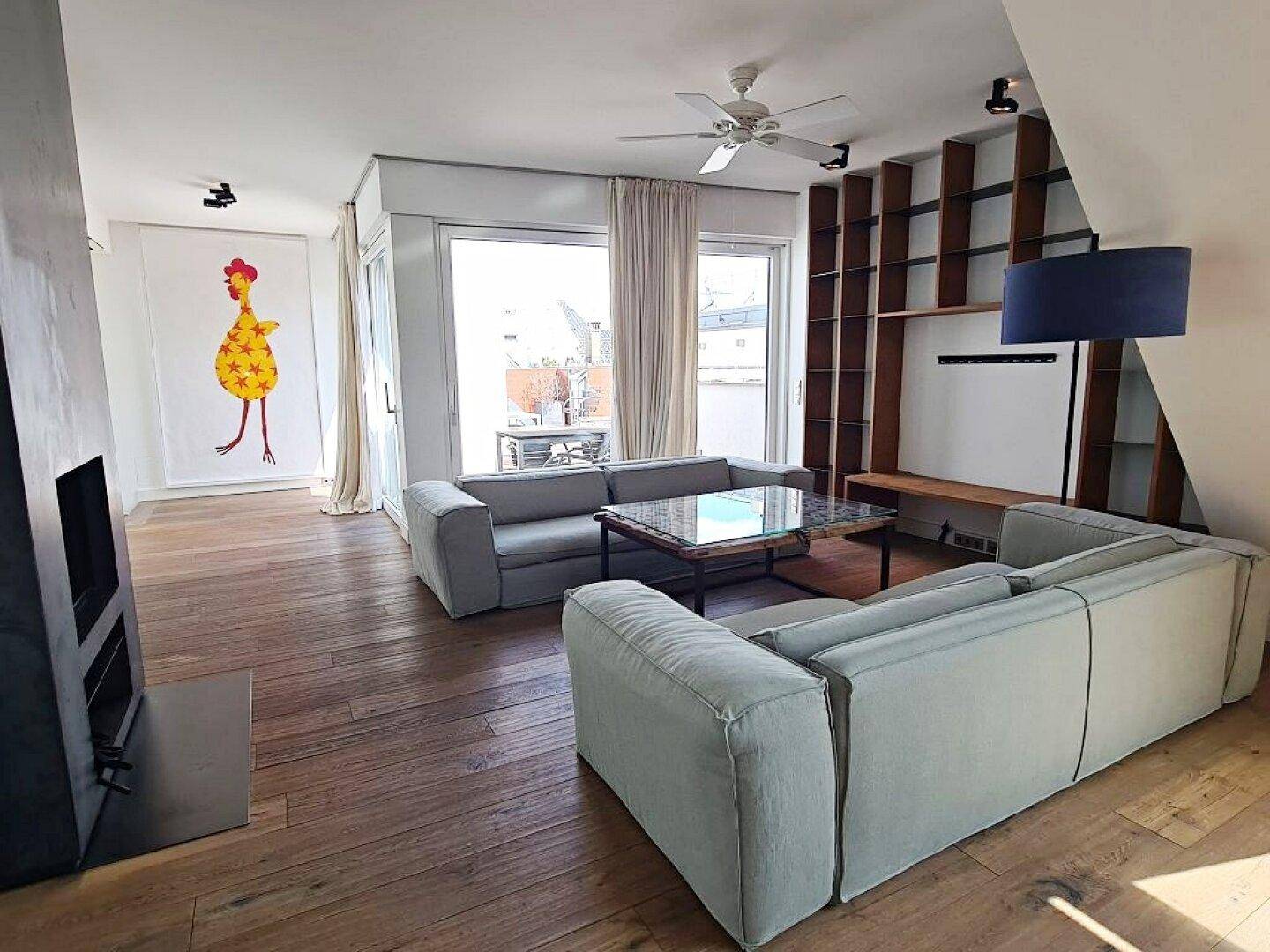 Offener Wohnbereich mit Holzboden, Kamin und Zugang zu einem Balkon oder einer Terrasse.