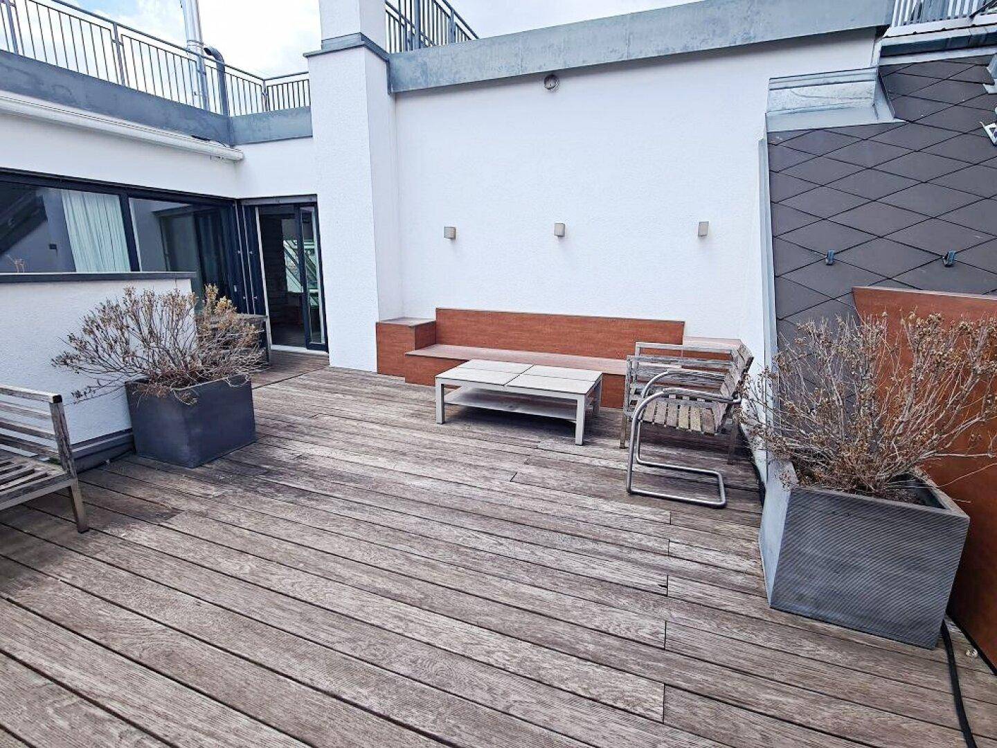 Geräumige Dachterrasse mit Holzdeck, Sitzgelegenheiten und Pflanzenkübeln.