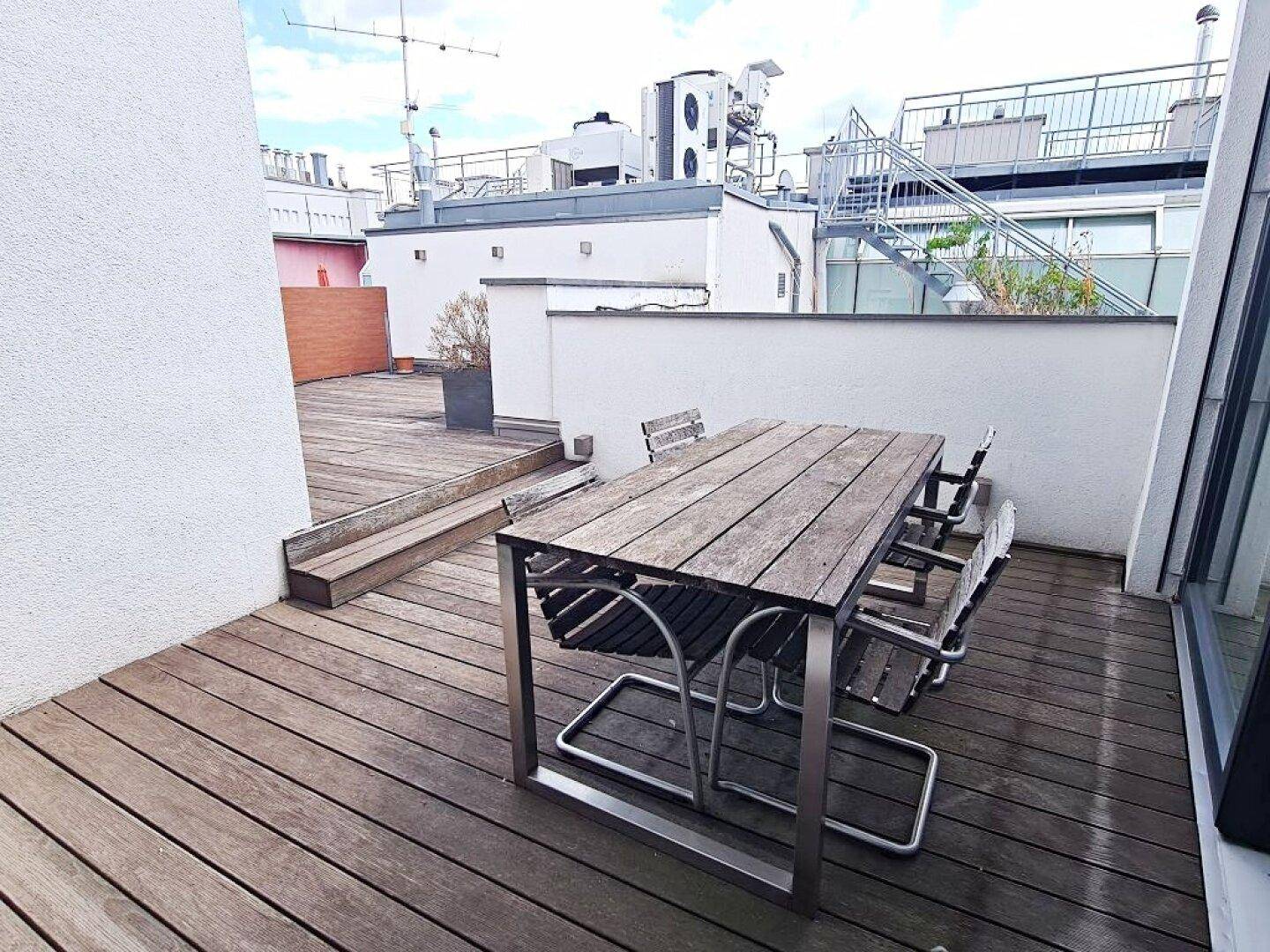 Dachterrasse mit Holztisch und Stühlen, umgeben von einer modernen Architektur.