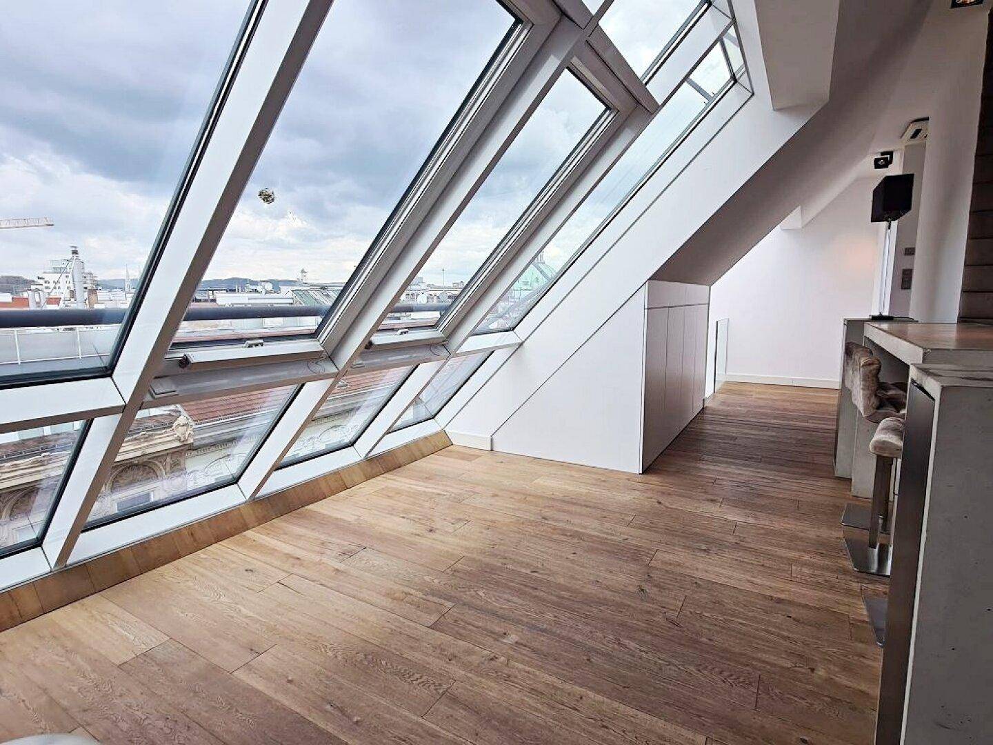 Heller Küchenbereich mit Dachschrägen, großen Fenstern und Holzboden.