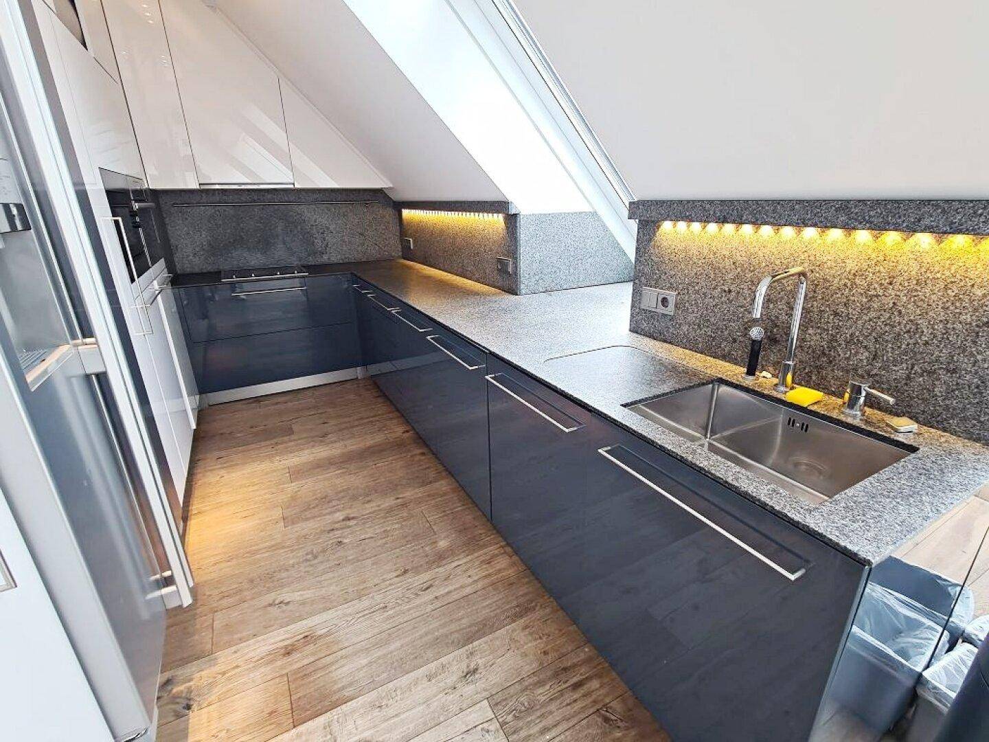 Moderne Einbauküche mit grauen Fronten, Granitarbeitsplatten und Dachfenstern.