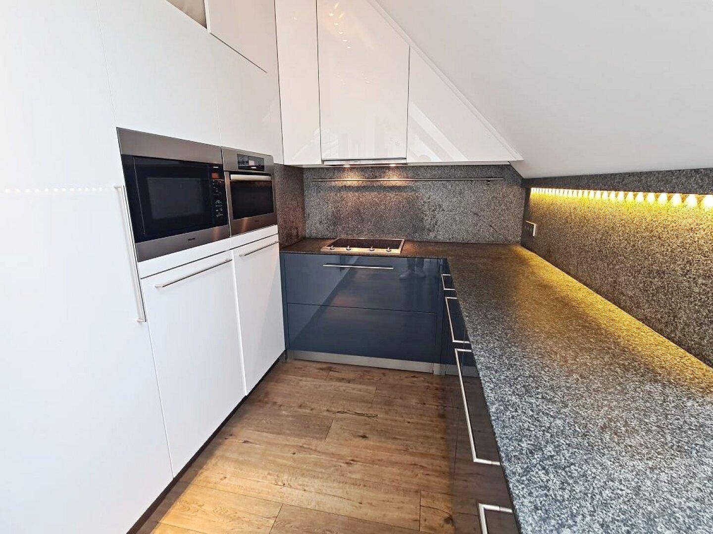 Moderne Küche mit weißen und dunkelgrauen Schränken, Granitarbeitsplatte und integrierten Geräten unter Dachschräge.