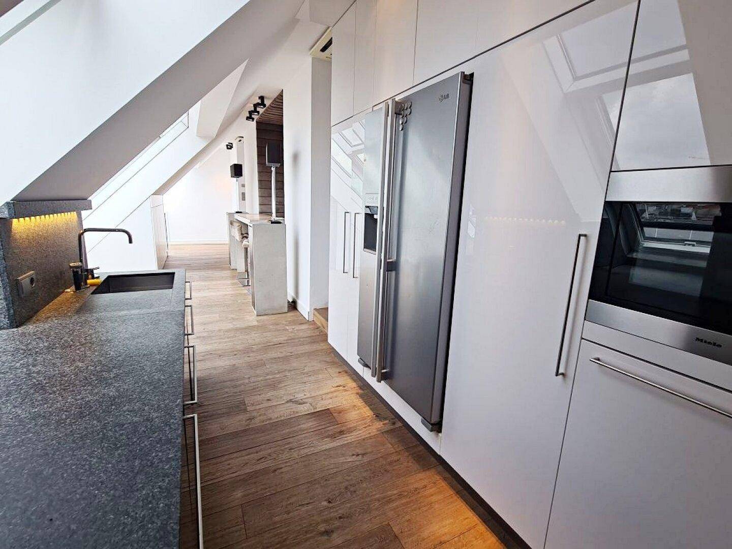 Blick auf die moderne Küche mit großem Kühlschrank, Holzfußboden und Dachfenstern in der Dachschräge.