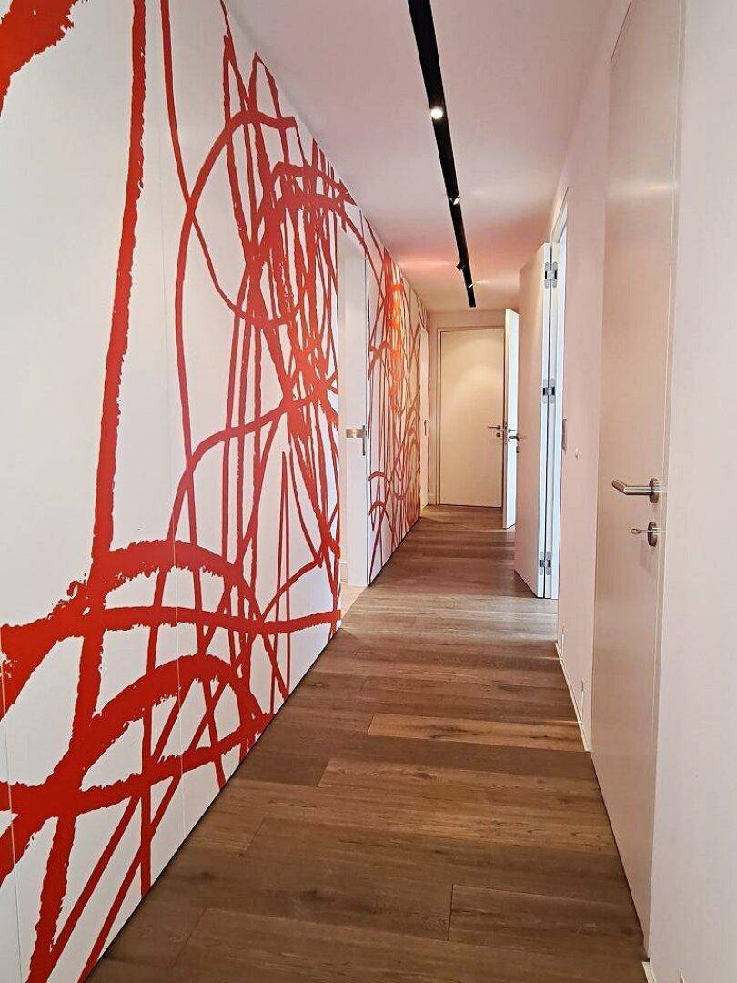 Moderner Flur mit auffälliger roter Wandgestaltung, weißen Türen und elegantem Holzfußboden.