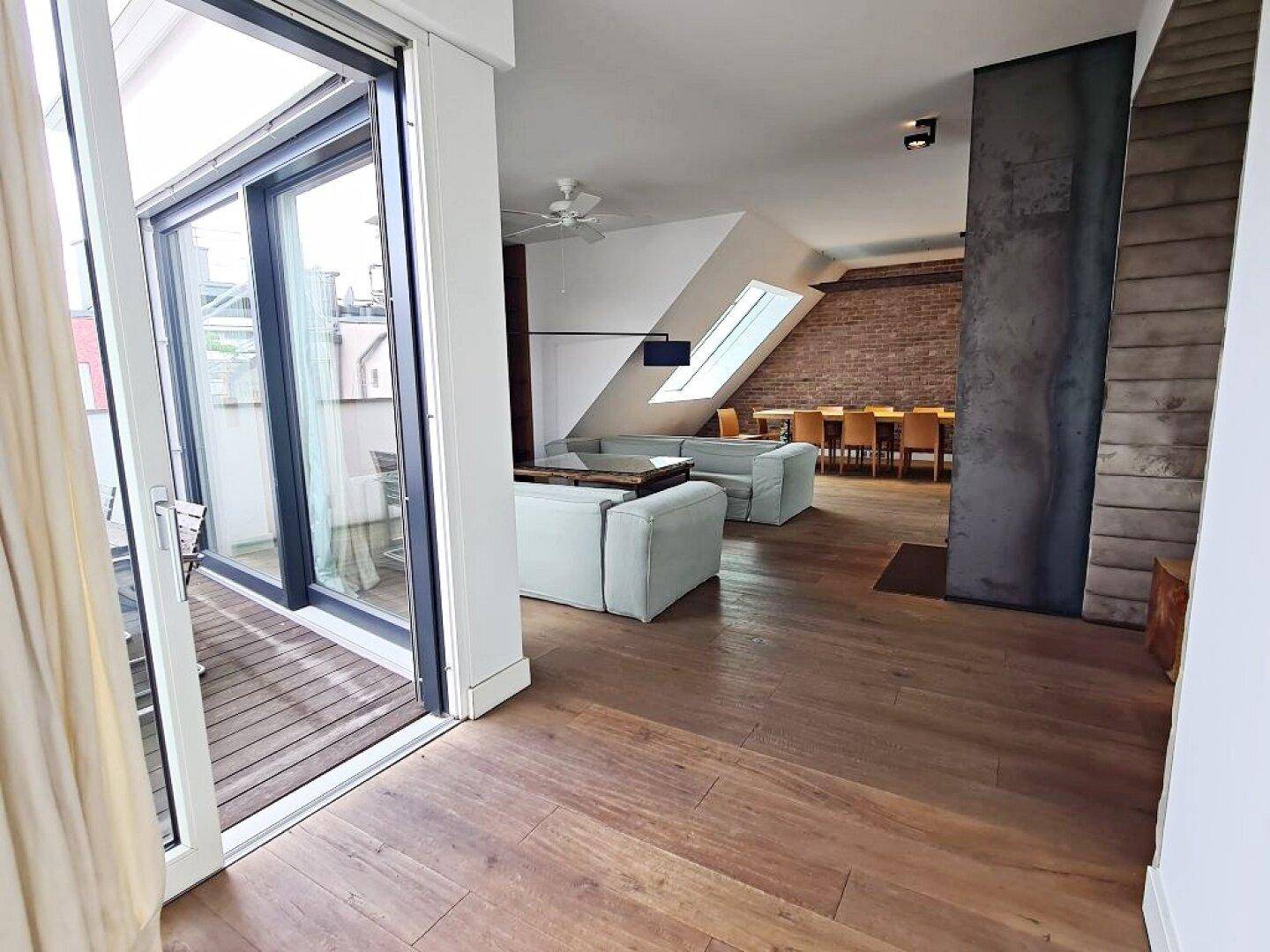 Geräumiger Wohn-Essbereich mit Holzboden, bequemen Sofas und Zugang zu einer Außenterrasse.