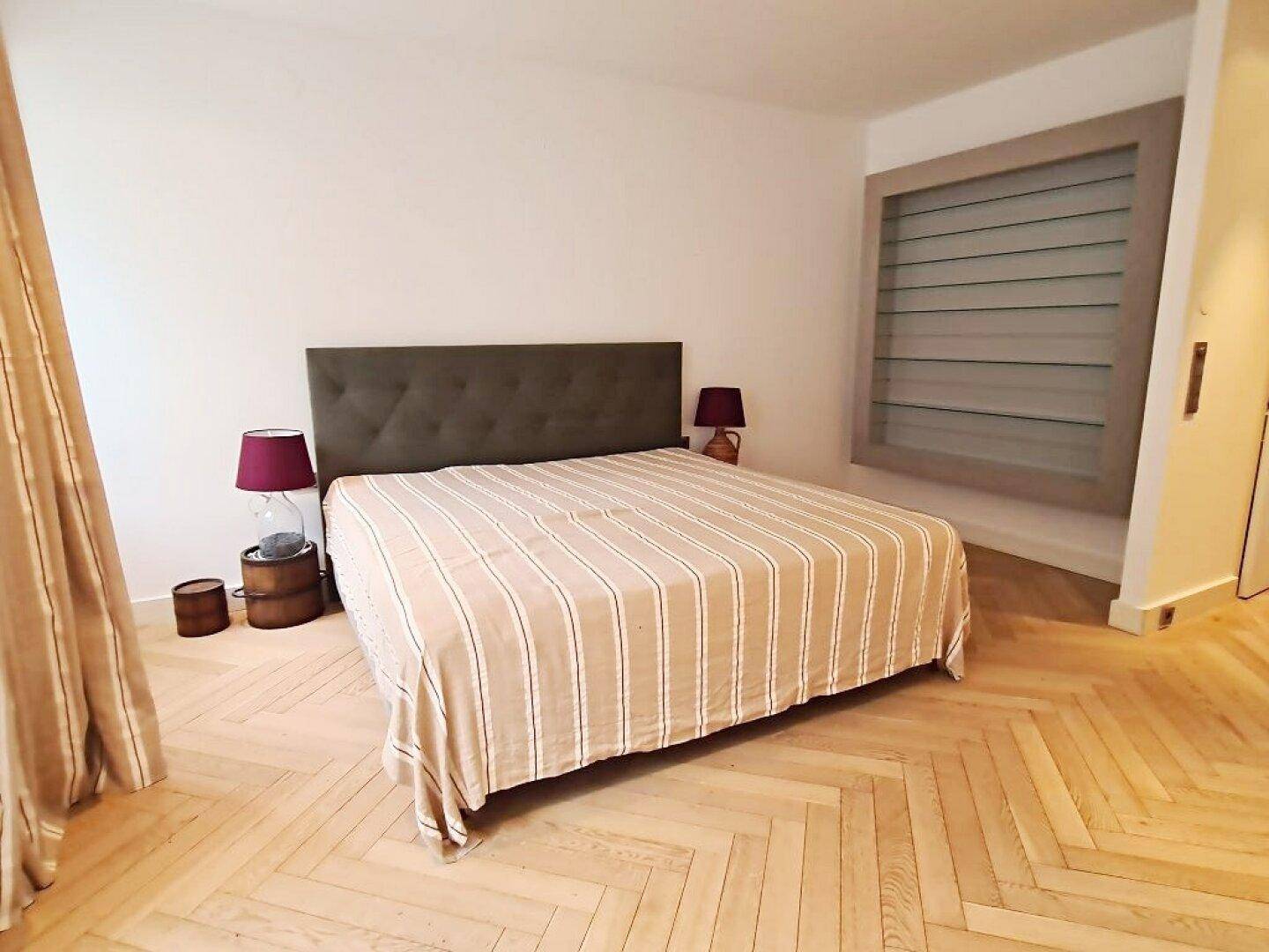 Schlafzimmer mit Fischgrätparkett, großem Bett und einer stilvollen Wanddekoration.