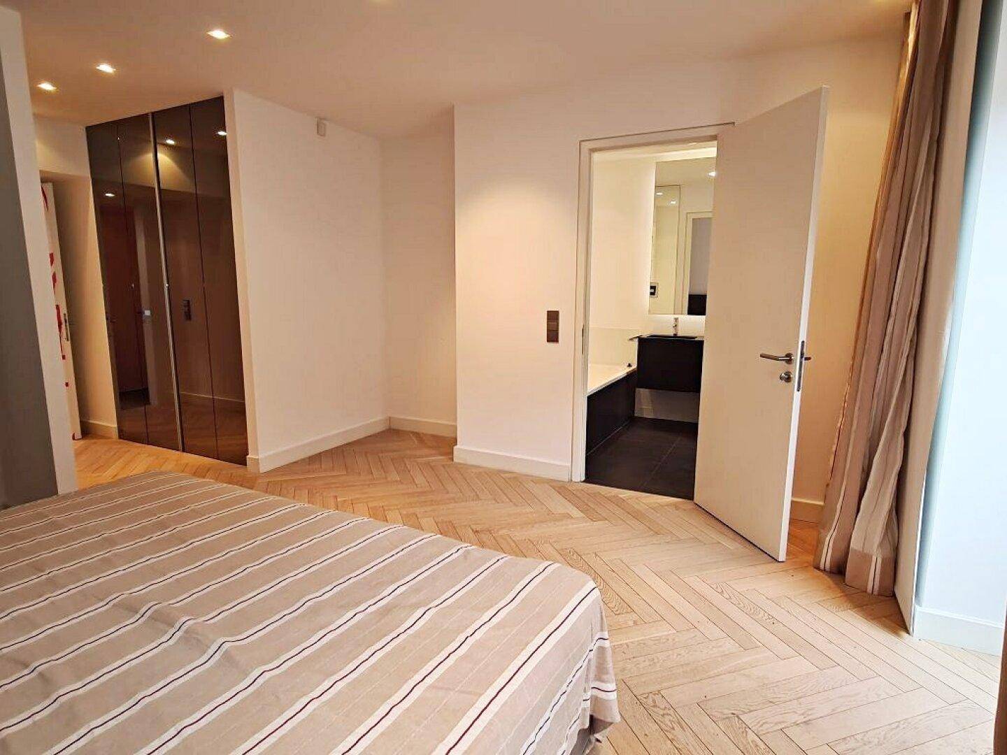 Schlafzimmer mit Fischgrätparkett, Spiegelschränken und direktem Zugang zu einem modernen Badezimmer.