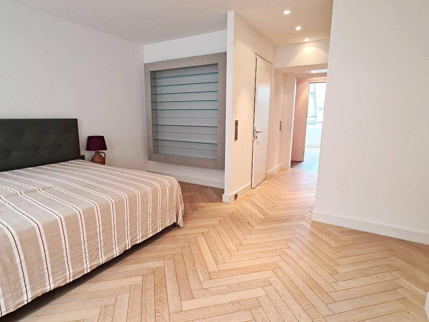 Geräumiges Schlafzimmer mit Fischgrätparkett und offenem Übergang zu einem hellen Flurbereich.