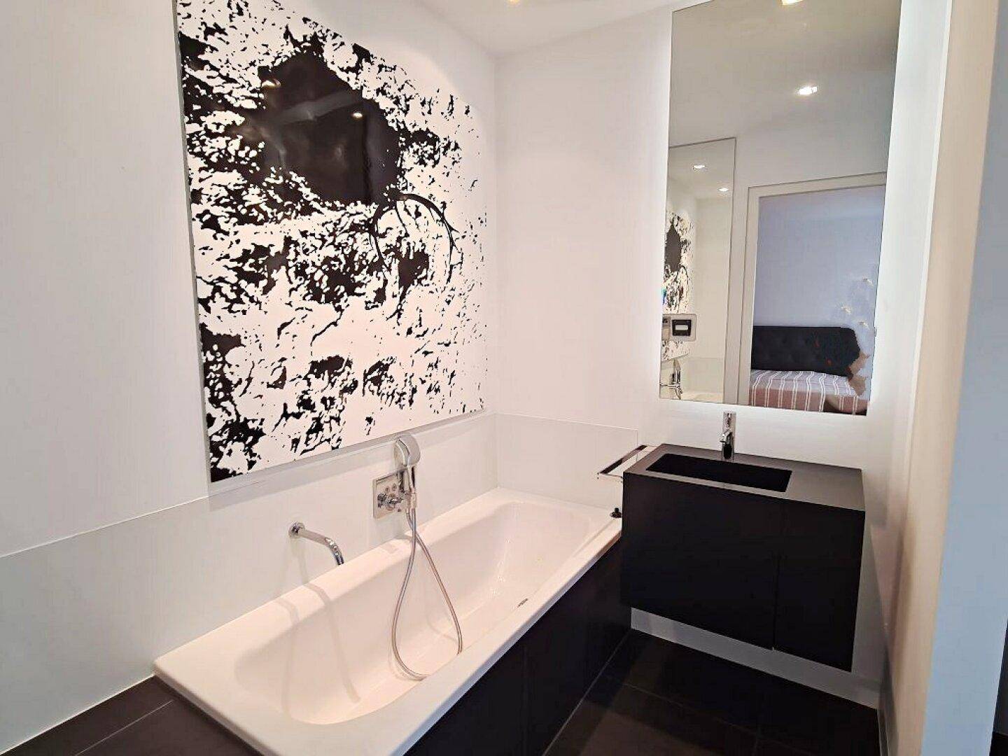 Modernes Badezimmer mit Badewanne, schwarzem Waschtisch und auffälligem Schwarz-Weiß-Kunstwerk.