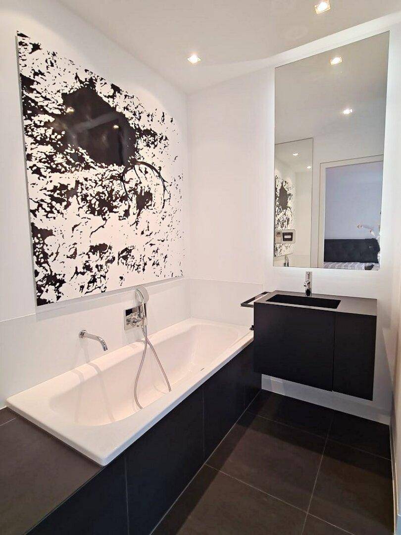 Stilvolles Badezimmer mit Badewanne, schwarzem Waschtisch und großem, modernem Kunstwerk an der Wand.