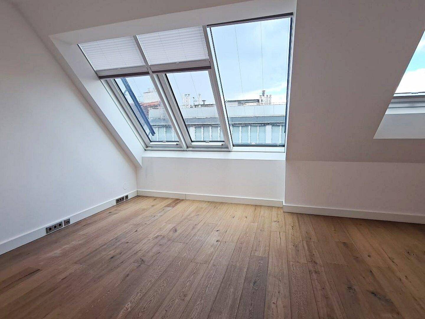 Heller Raum mit Holzboden, Dachschräge und großen Dachfenstern für viel Tageslicht.