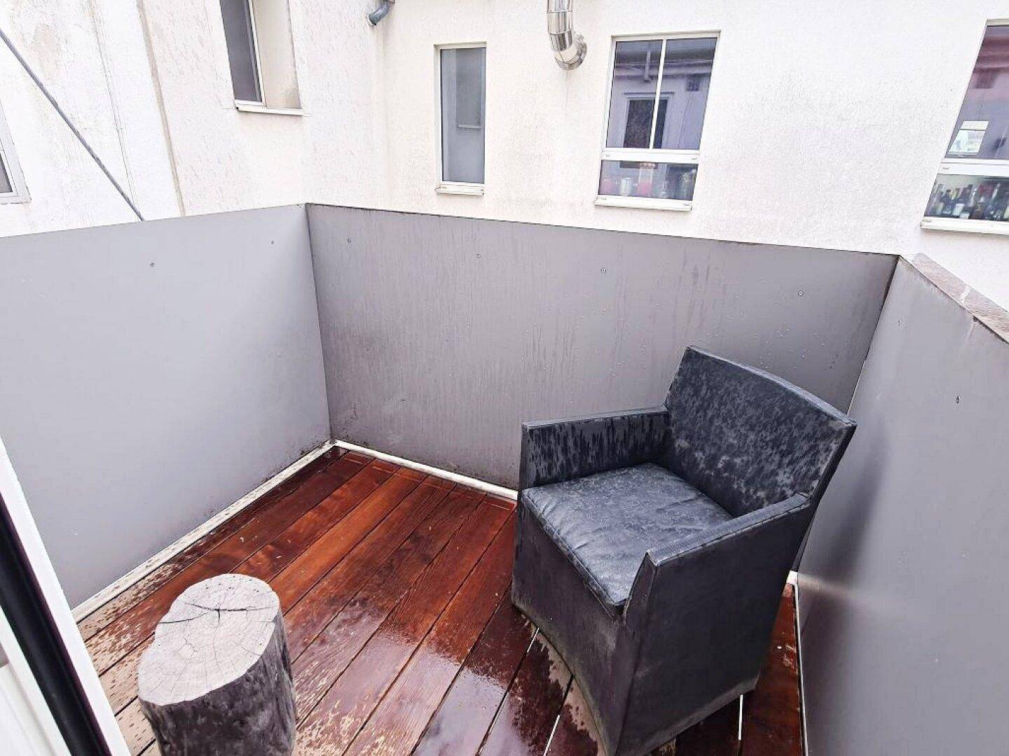 Kleiner Außenbalkon mit Holzbelag und einem einzelnen Stuhl, ideal für eine kurze Pause.