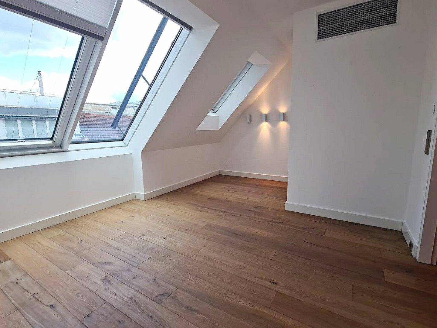 Geräumiger Raum mit Holzboden, Dachschräge, Dachfenstern und indirekter Wandbeleuchtung.