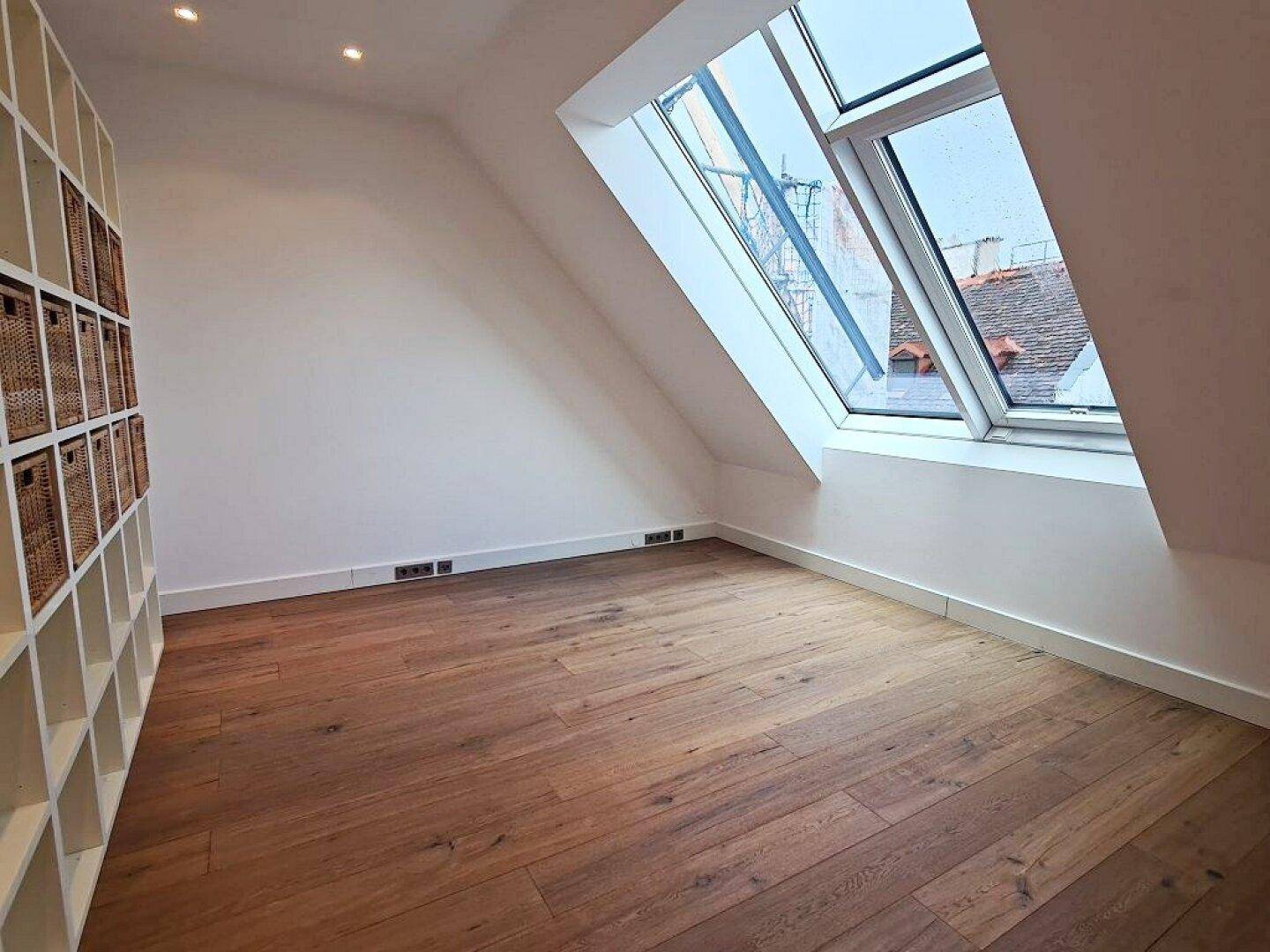 Heller Raum mit Holzboden, Dachschräge, Dachfenster und einem großen weißen Regalsystem.