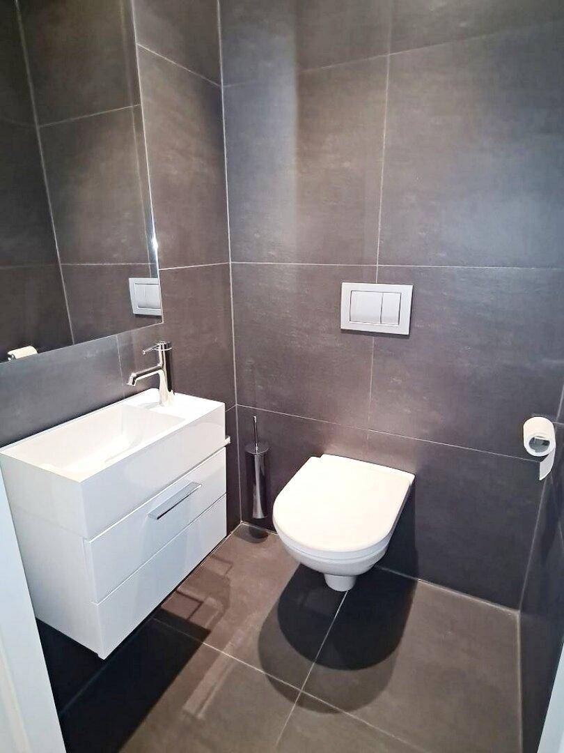 Modernes Gäste-WC mit dunklen Fliesen, wandhängendem WC und weißem Waschtisch.