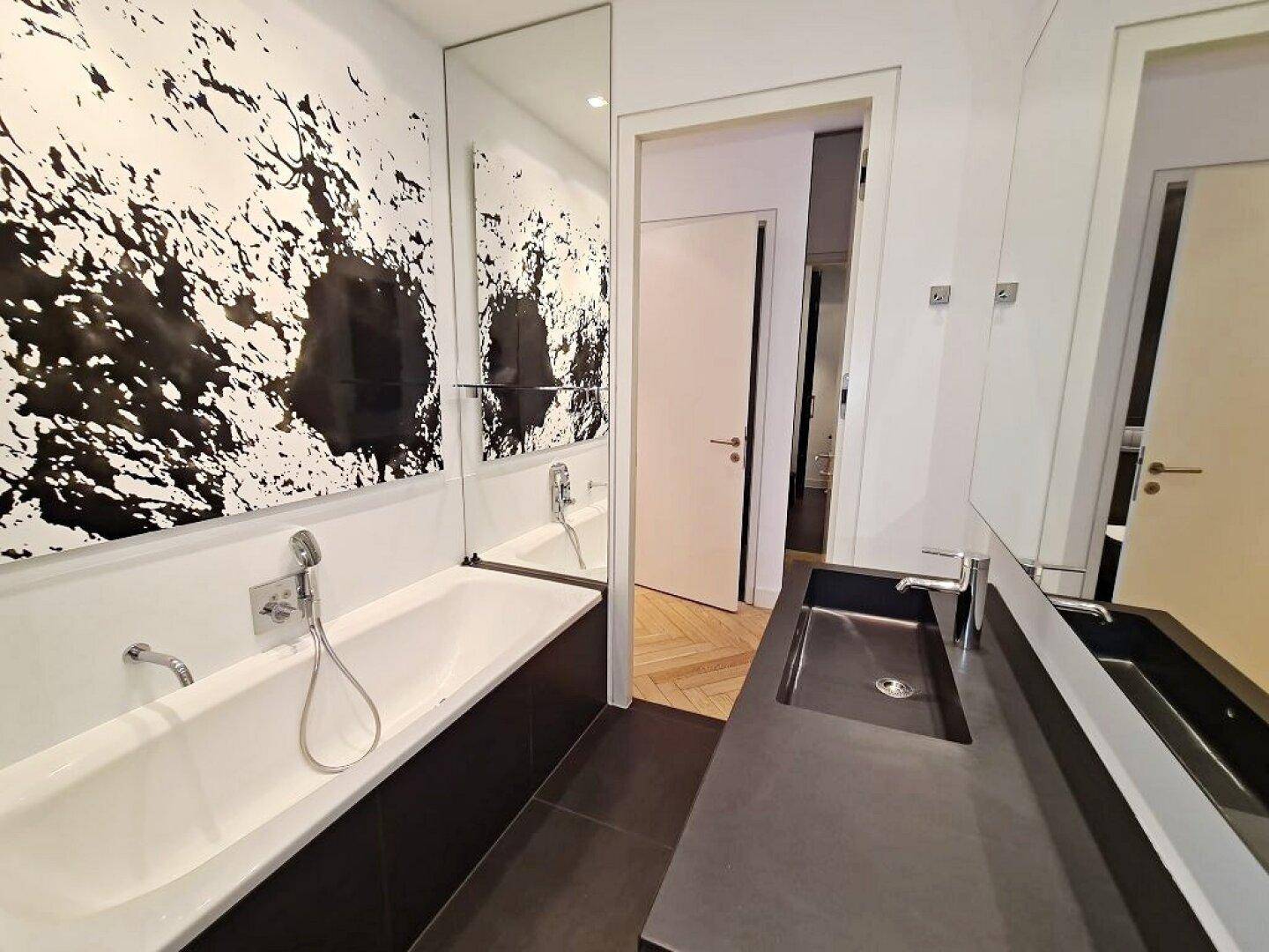 Stilvolles Badezimmer mit integrierter Badewanne und Waschtisch, angrenzend an einen Raum mit Parkett.