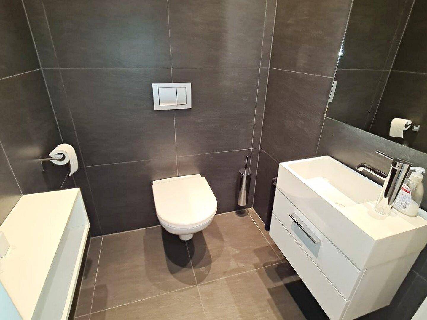 Helles Gäste-WC mit dunklen Wandfliesen, wandhängender Toilette und modernem Waschtisch.