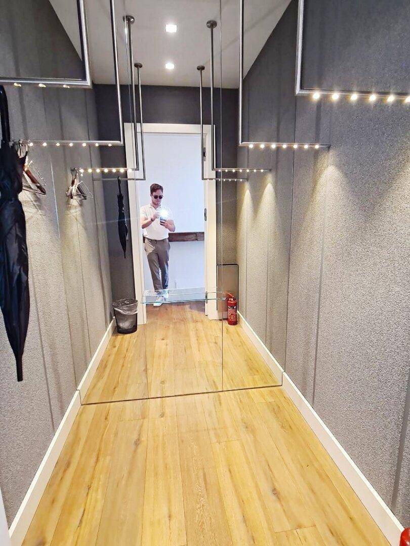 Moderner Flur mit Spiegelwänden, Holzfußboden und integrierter Beleuchtung, die den Raum erweitert.