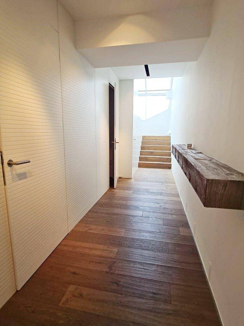 Geräumiger Flur mit Holzfußboden, weißen Wänden und einer Holzablage, die zu einer Treppe führt.
