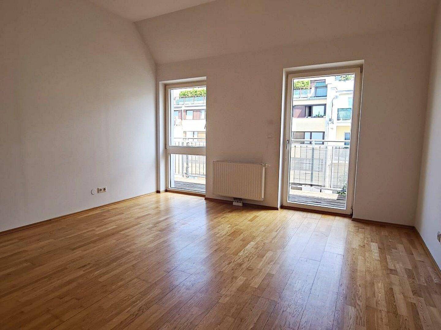 Lichtdurchflutetes Wohnzimmer mit Parkettboden und zwei Fenstertüren zum Balkon.