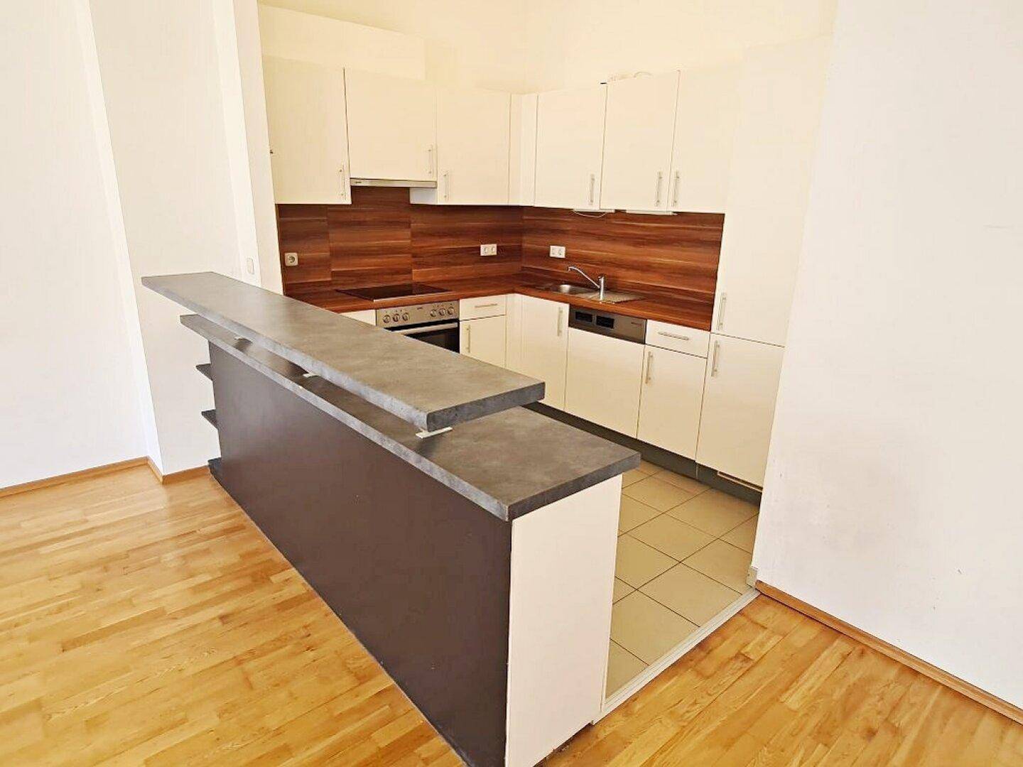 Moderne Einbauküche mit weißen Schränken, Holzoptik und praktischer Frühstückstheke.