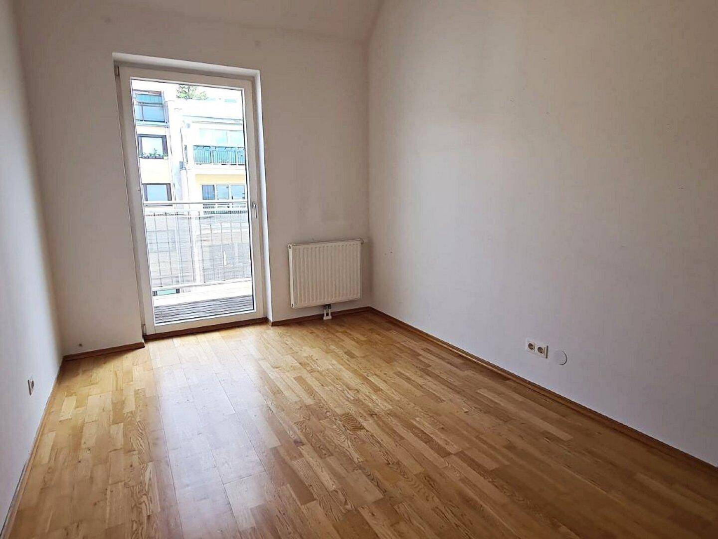 Helles Zimmer mit Parkettboden und Zugang zu einem französischen Balkon.