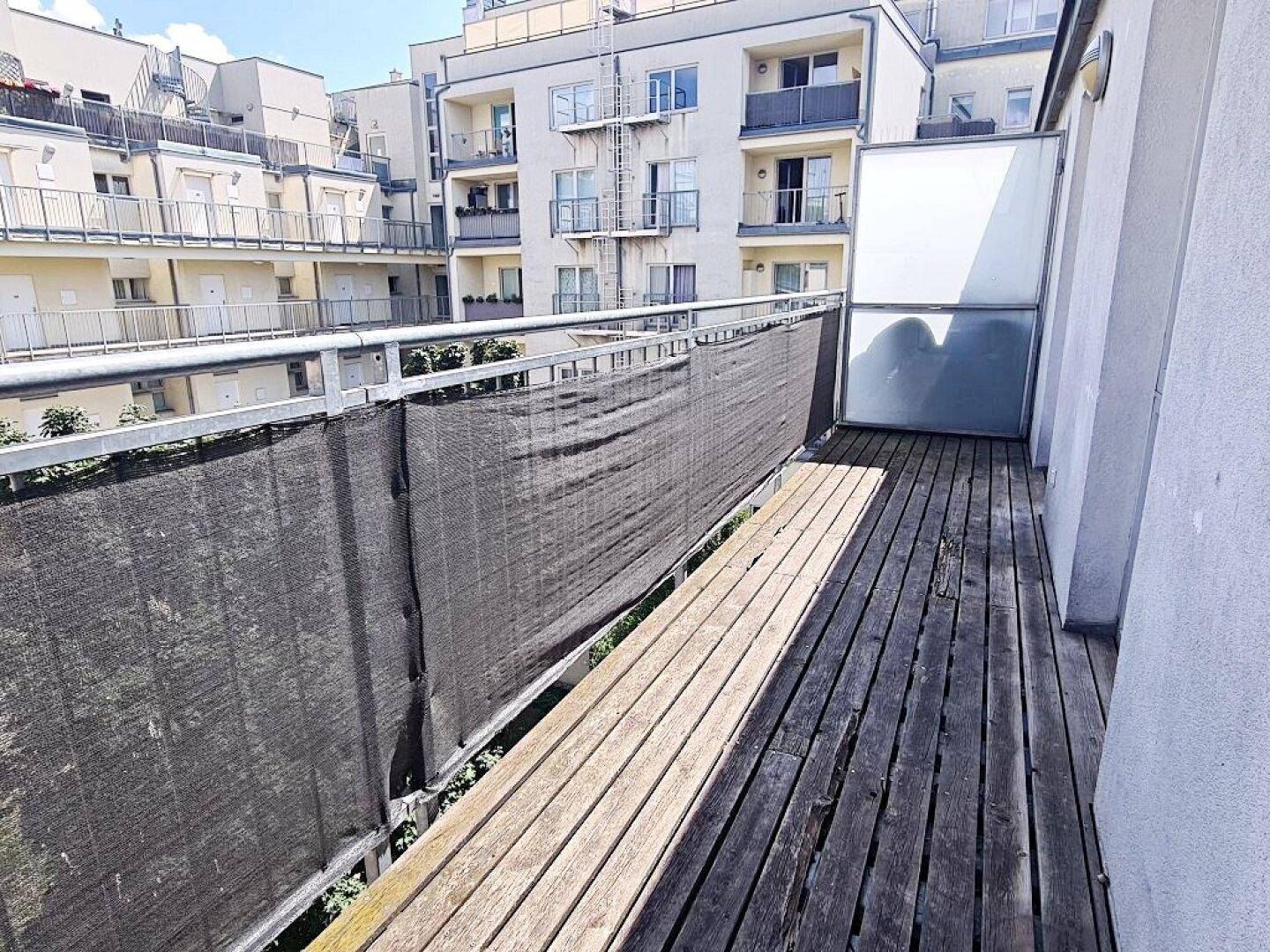 Langer Balkon mit Holzbelag und Blick auf den Innenhof der Wohnanlage.
