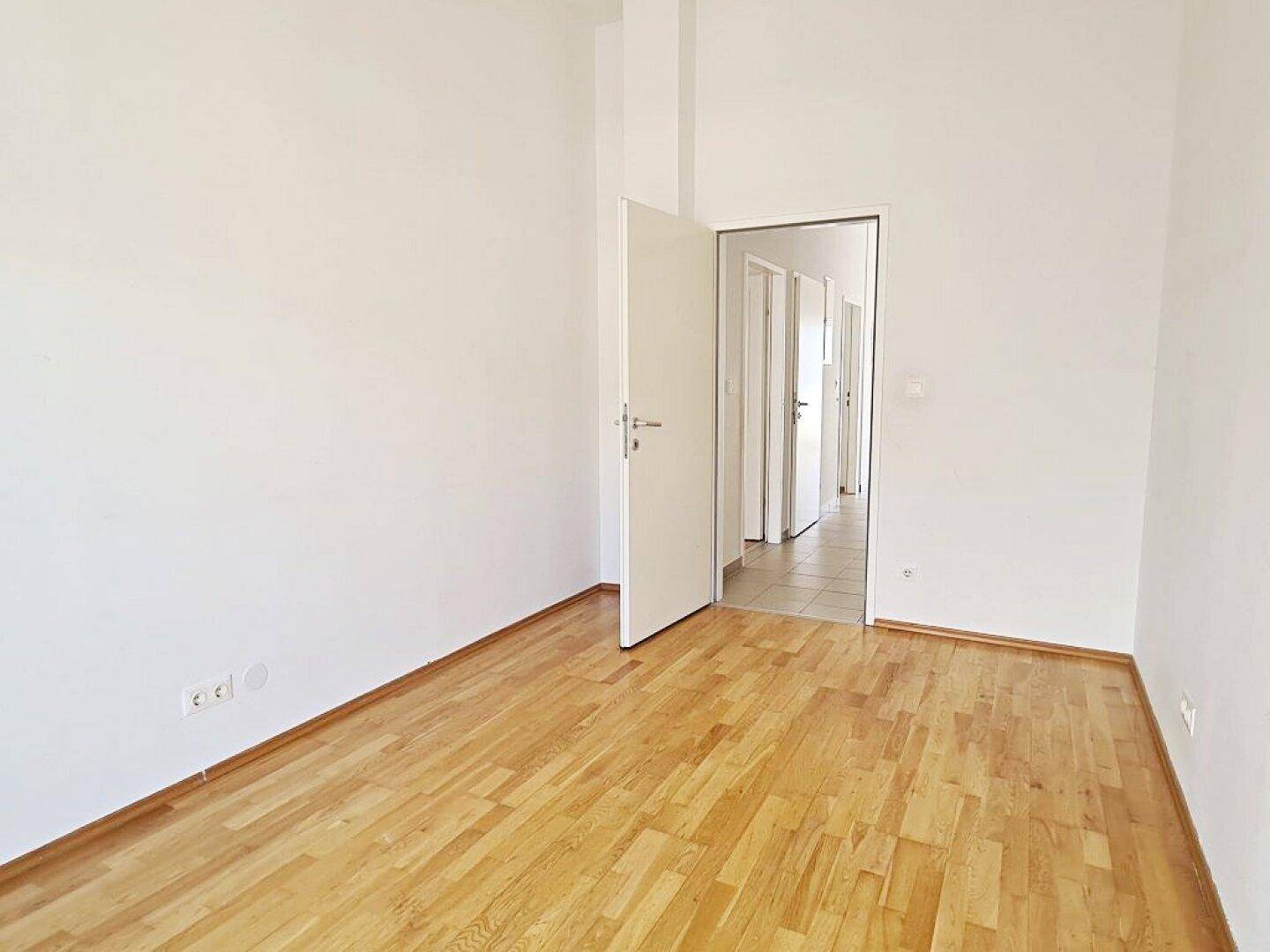 Geräumiges Zimmer mit Parkettboden und Blick in den hellen Flur.