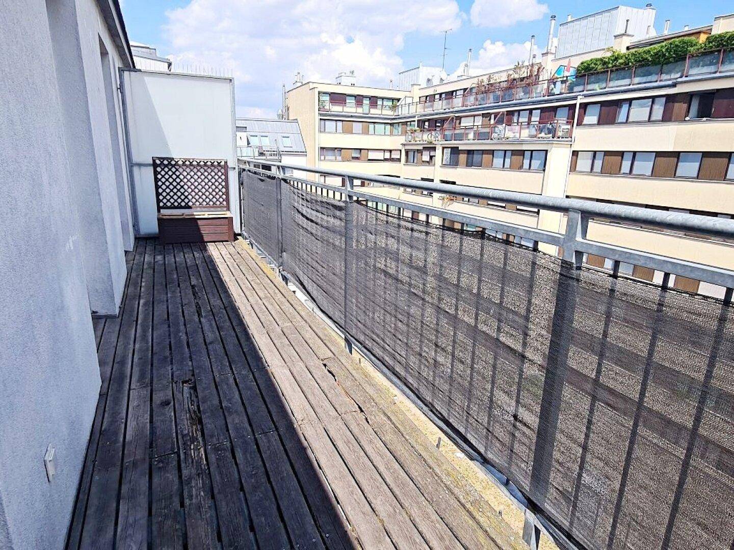 Sonniger Balkon mit Holzbelag und weitem Blick über die Dächer der Stadt.