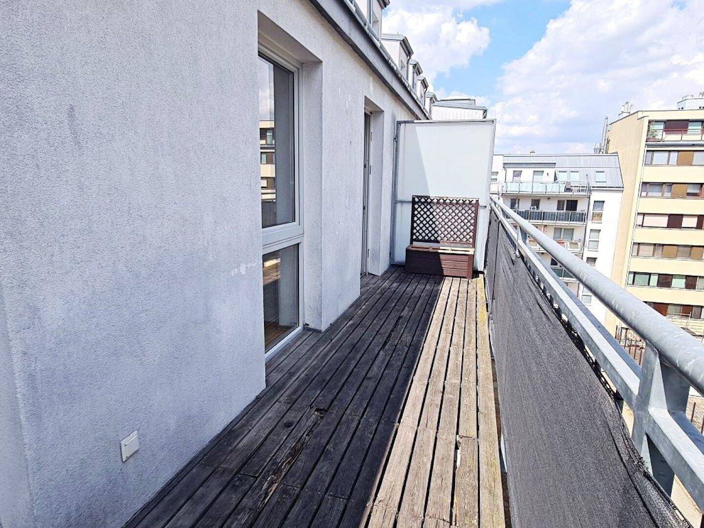 Geräumiger Balkon mit Holzplanken und Blick auf die Nachbargebäude.