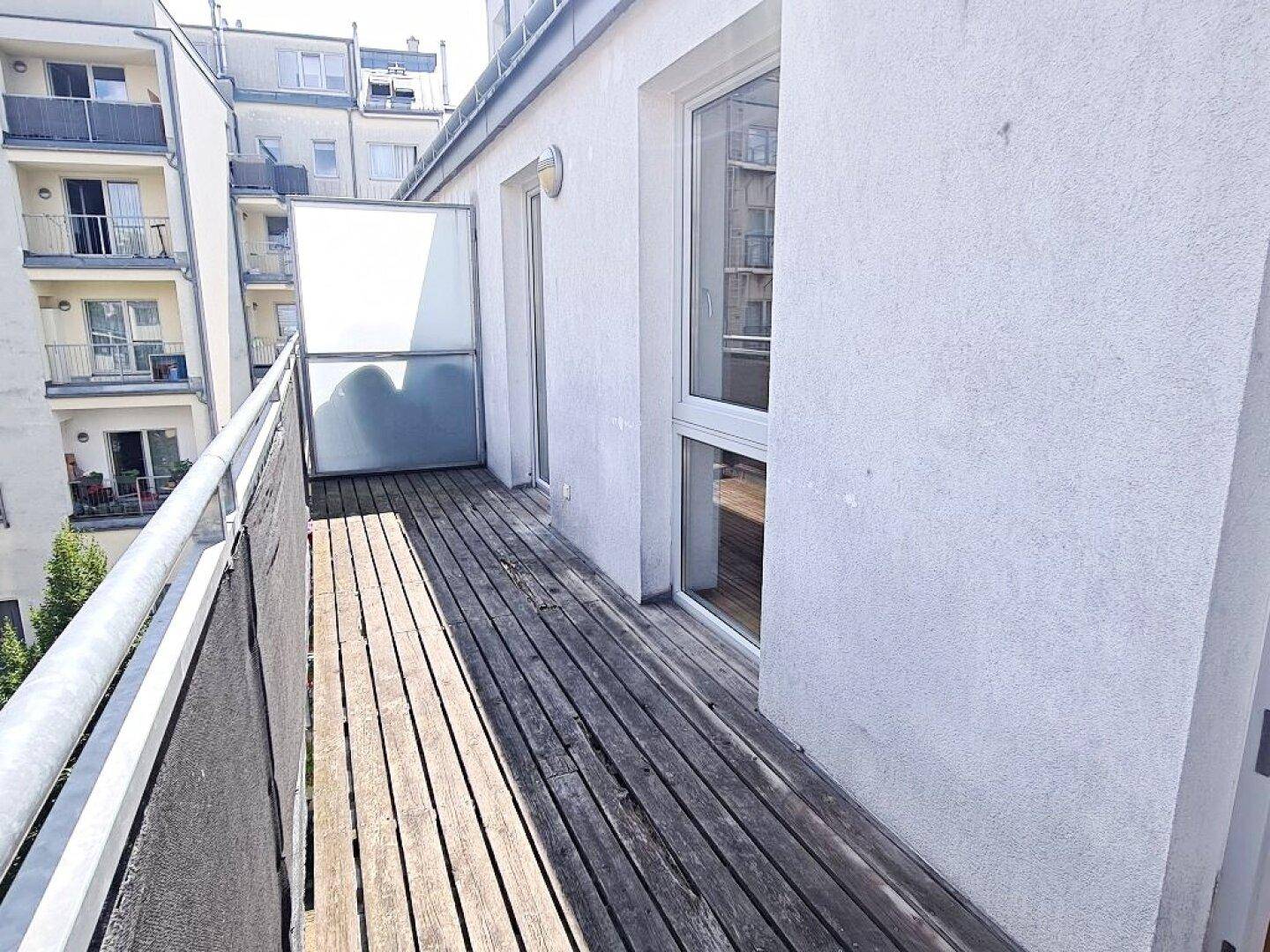 Heller Balkon mit Holzplanken und Blick auf die umliegenden Gebäude.