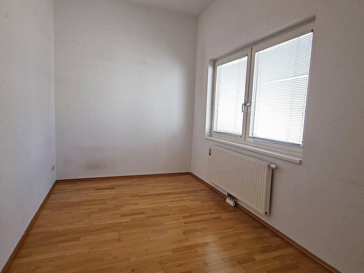 Ruhiges Zimmer mit Parkettboden und Fenster mit Jalousien für Privatsphäre.
