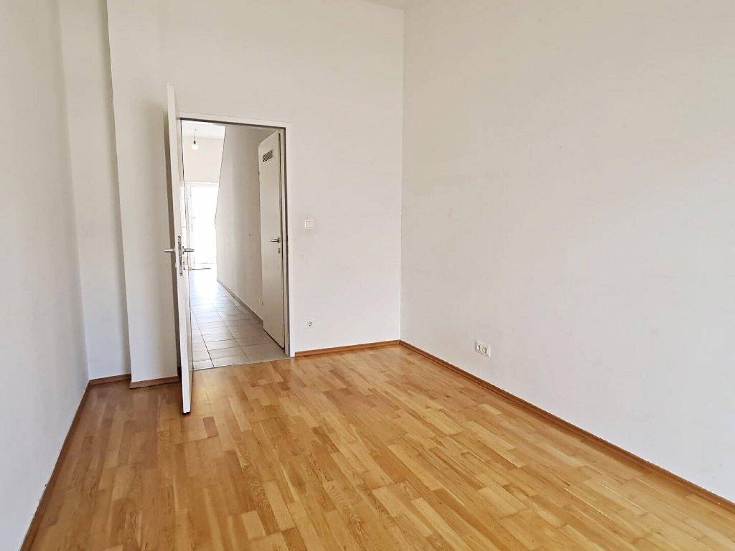 Helles Zimmer mit Parkettboden und Zugang zum gefliesten Flur.