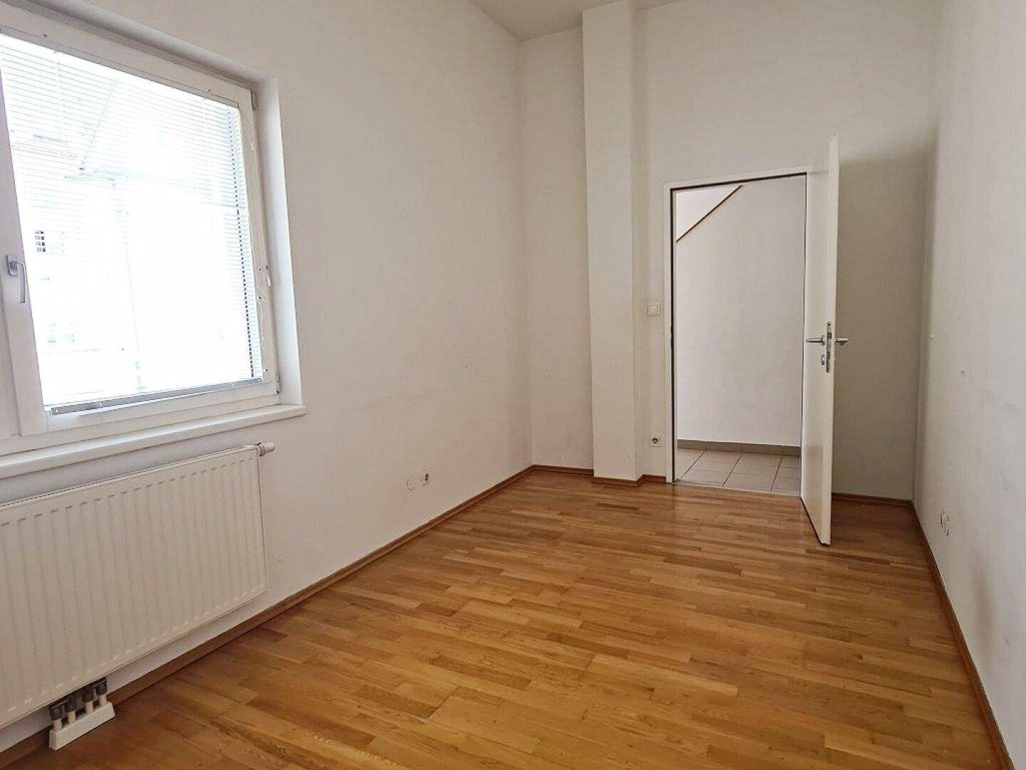 Helles Zimmer mit Parkettboden und Fenster mit Jalousien, bietet viel Licht.
