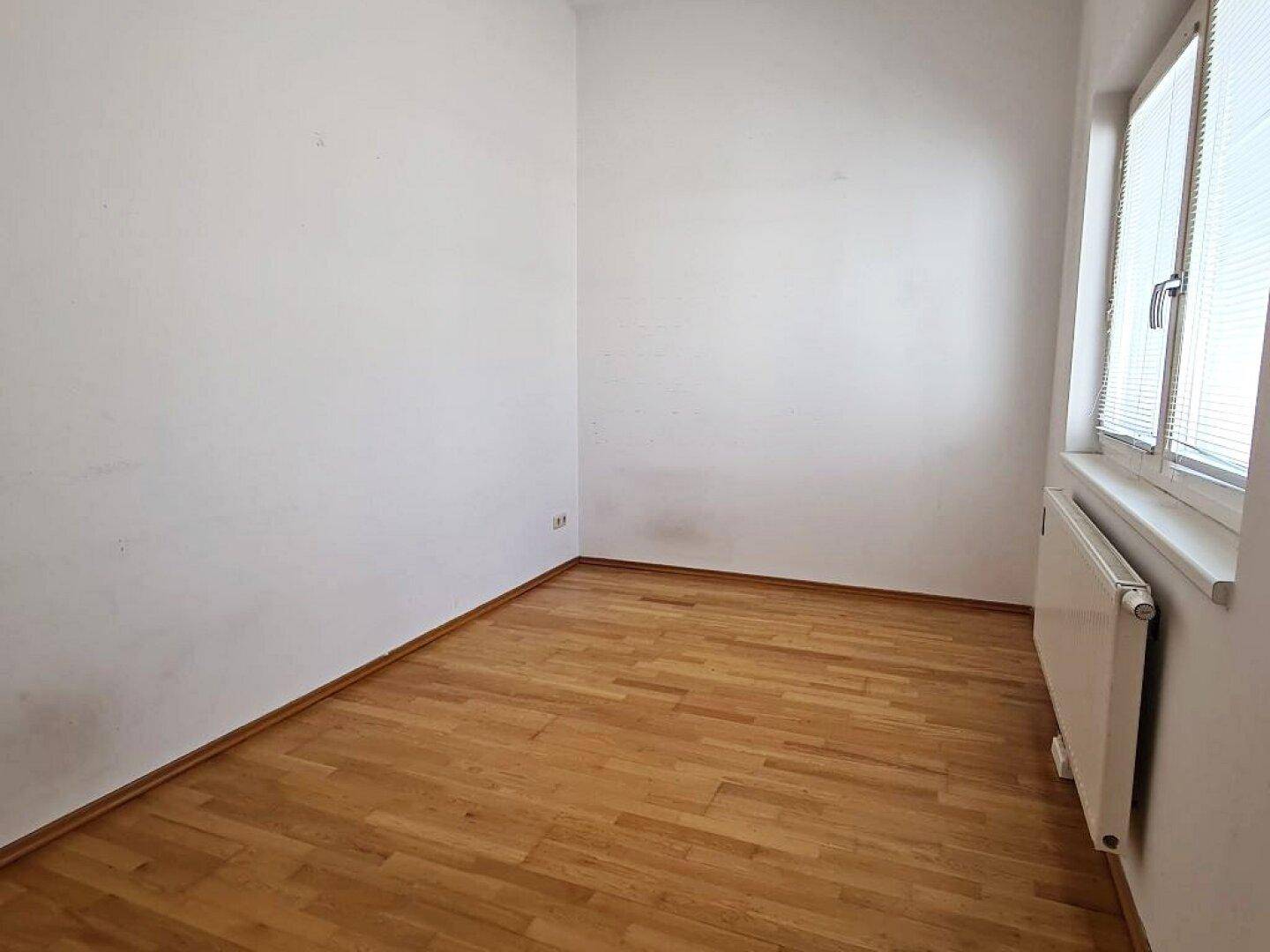 Gemütliches Zimmer mit Parkettboden und weiß gestrichenen Wänden, sehr hell.