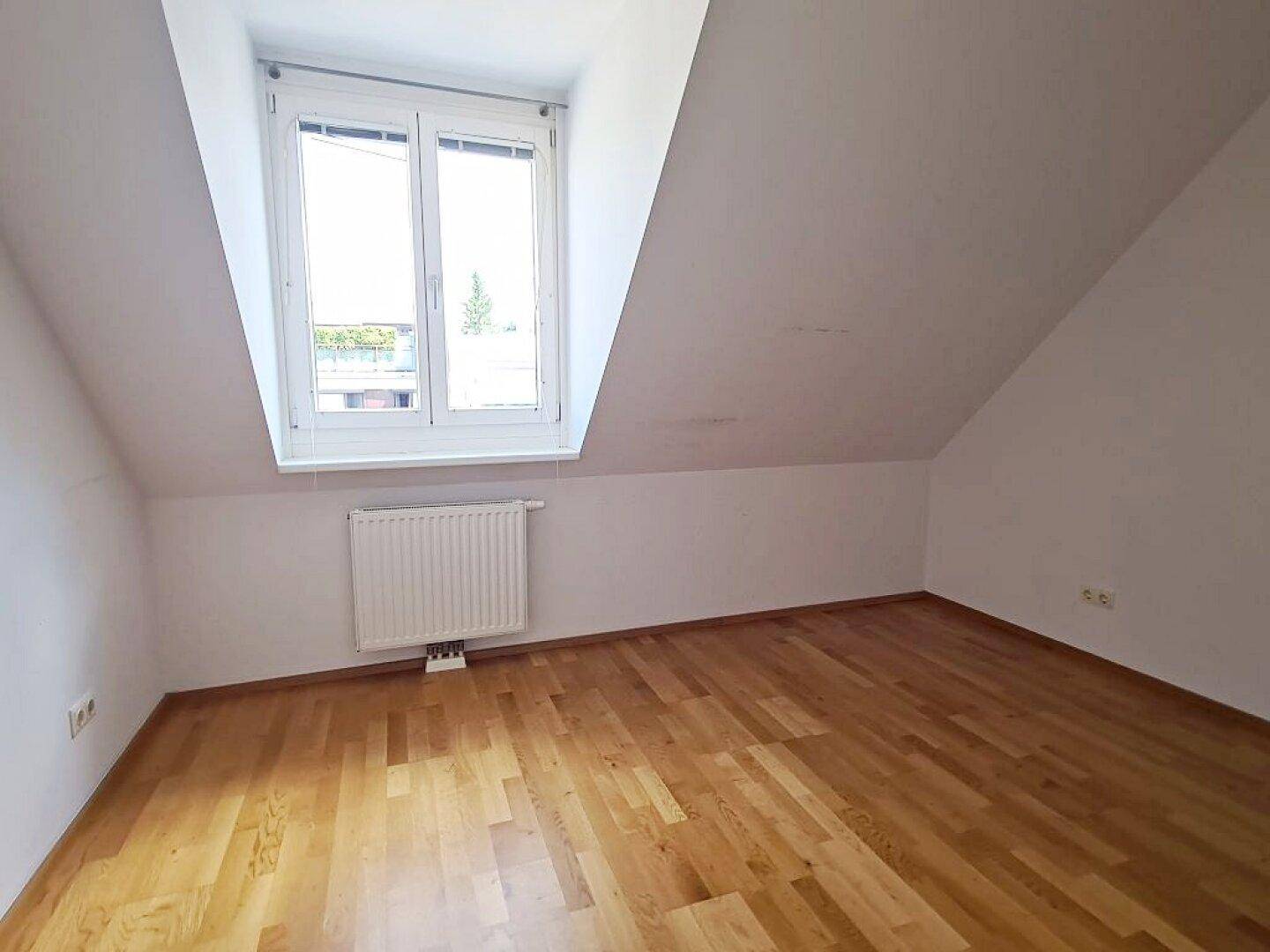 Dachzimmer mit Parkettboden, Dachschräge und Fenster für natürliches Licht.