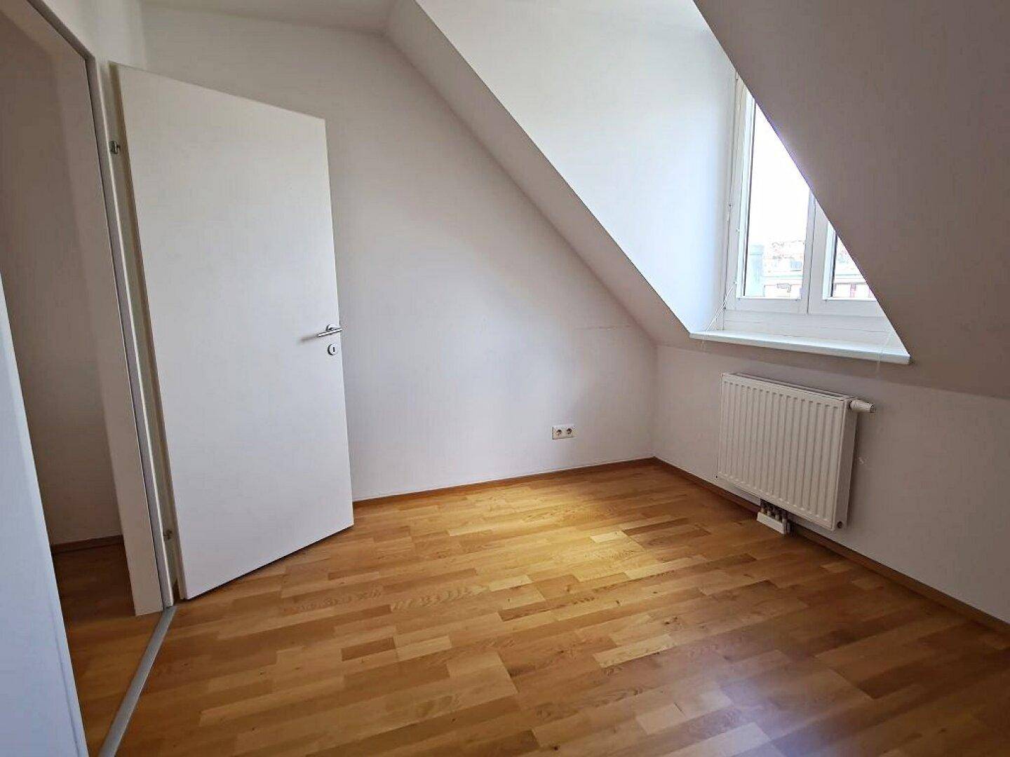 Helles Dachzimmer mit Parkettboden, Dachschräge und Fenster, sehr einladend.